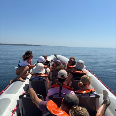 Group wearing life jackets seated in a boat on calm water under a clear blue sky.