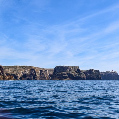 Rocky coastline with cliffs and a lighthouse under a clear blue sky.