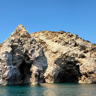 Rocky cliff with arch formations above a calm blue sea and clear sky.