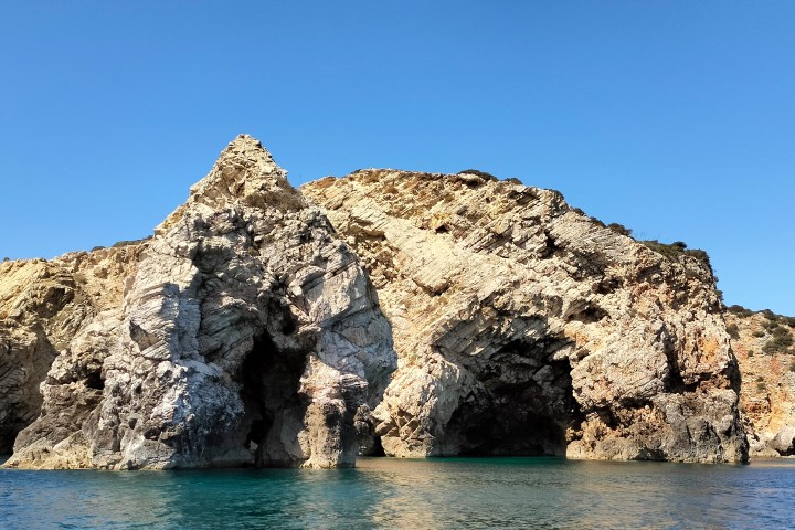 Rocky cliff with arch formations above a calm blue sea and clear sky.