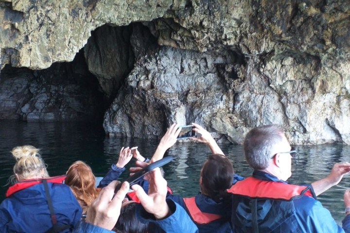 People in life vests taking photos of a cave from a boat.
