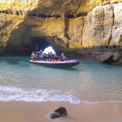 People in a boat entering a cave with turquoise water and rocky walls.