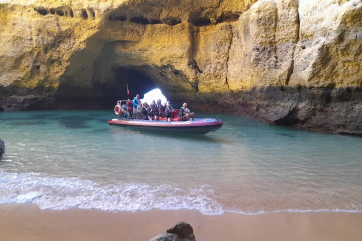 People in a boat entering a cave with turquoise water and rocky walls.