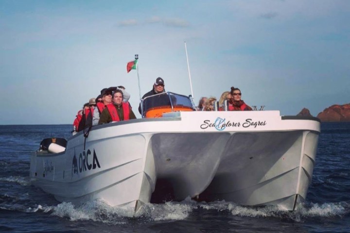 A group of people on a white boat named 'Sea Explorer Sagres' in the ocean under a clear sky.