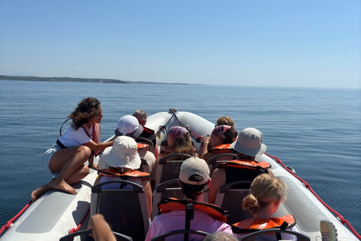 People wearing life vests seated in a boat on calm water, one person sitting on the edge.