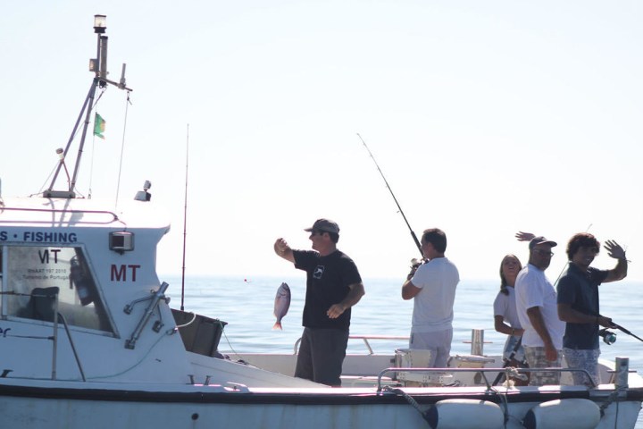 People fishing on a small boat in open water, one holding a fish.