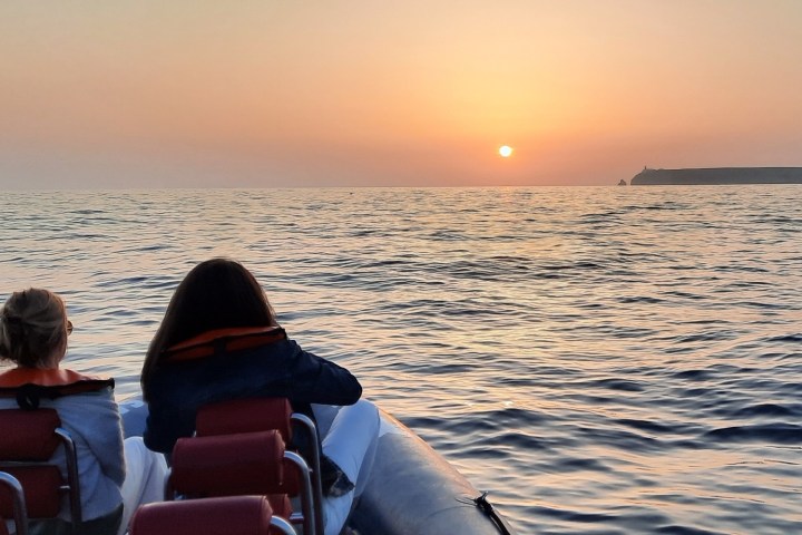 Two people on a boat watching the sunset over the sea.