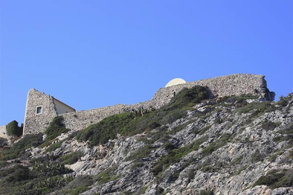 Stone wall and building on a rocky hillside under a clear blue sky.