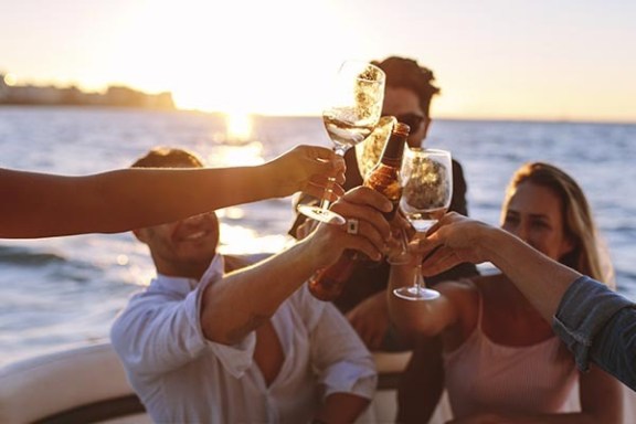 Group toasting with drinks on a boat at sunset.