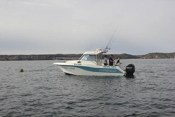 Motorboat on the water with people on board, fishing rods, and distant coastline.