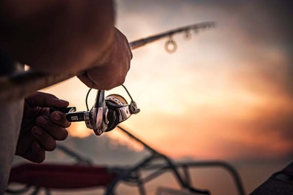 Close-up of hands holding a fishing rod with a blurred sunset in the background.