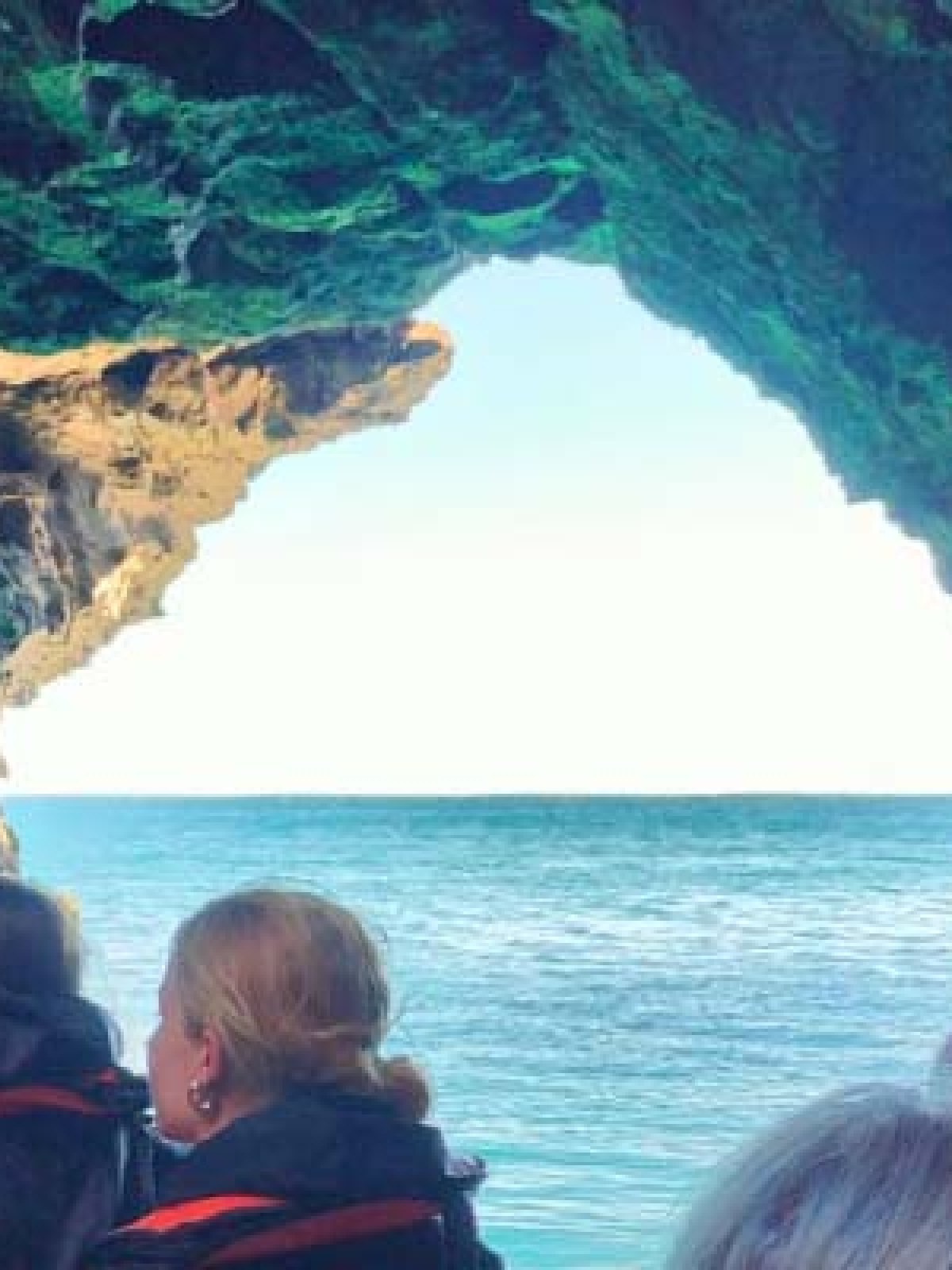 People in a boat approaching an ocean cave with a view of the sea.