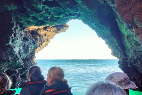 People in a boat approaching an ocean cave with a view of the sea.